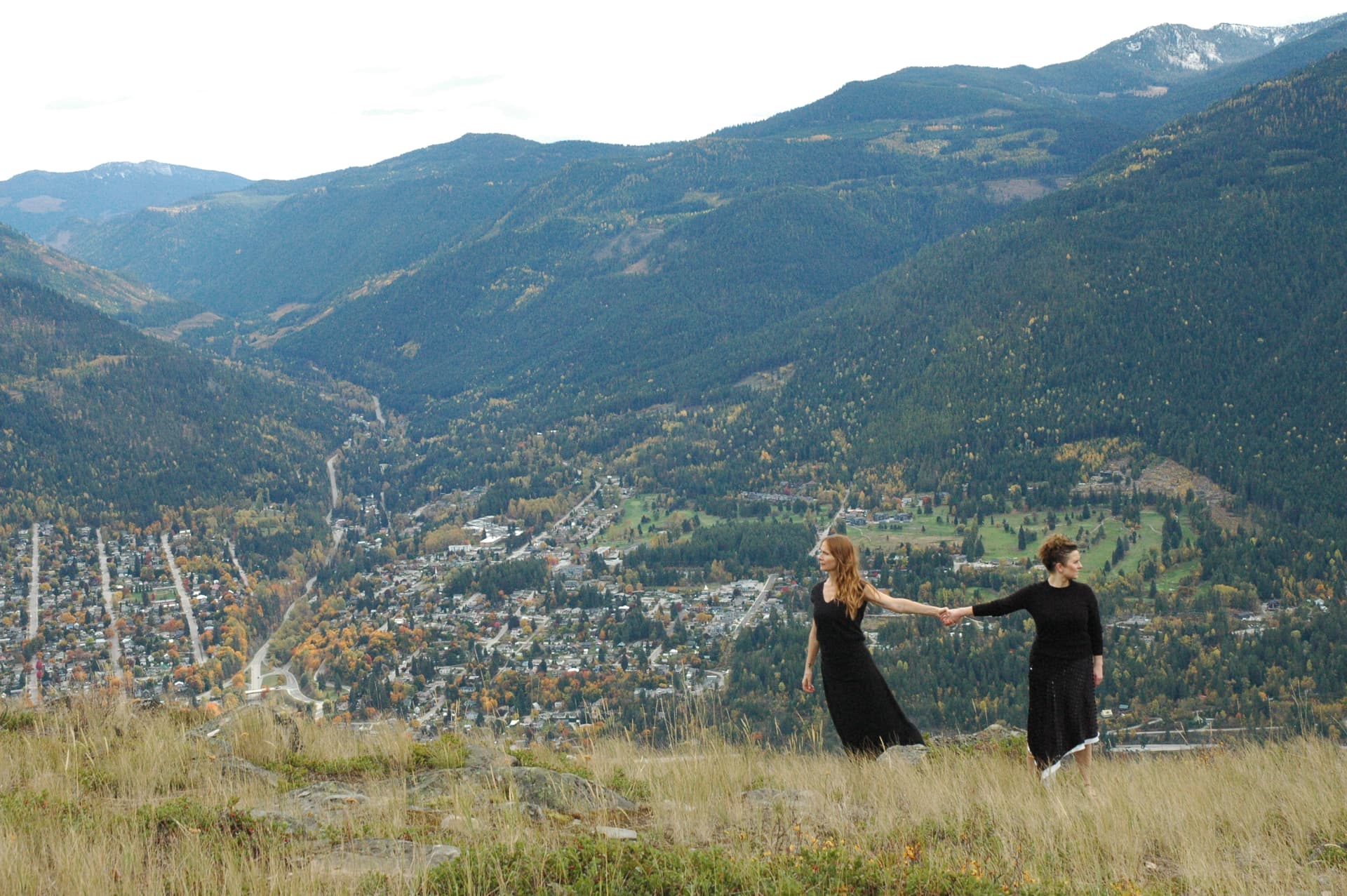 Two performers holding hands on a grassy hilltop above a mountain valley